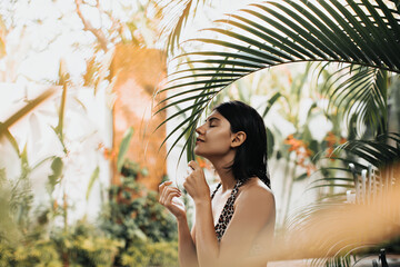 Selective focus of gorgeous girl with tattoo enjoying vacation. Brunette european lady touching palm tree leaf on nature background.