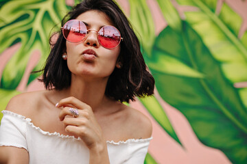 Refined woman in pink sunglasses posing with kissing face expression. Young lady expressing love in front of green graffiti.