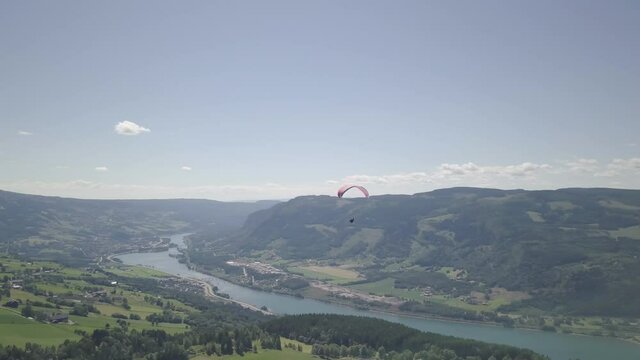 Aerial view of a parasailer above fields, river and forest, in Norway - pan, drone shot