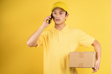 Portrait of delivery male holding cargo box and listening to phone on yellow background