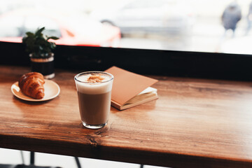 Cup of coffee, croissant, notebook at table in cafe. Blurred background