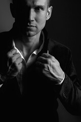 A strong, confident man adjusts the collar of his jacket and looks at the camera. Portrait. Black and white photo