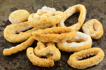 Frozen breaded calamari rings with ice crystals on weathered baking pan