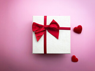 Valentine gift with pink bow and two mini hearts on pink background.