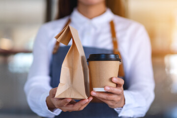 Closeup of a waitress holding and serving paper cup of coffee and takeaway food in paper bag to customer in a shop - Powered by Adobe