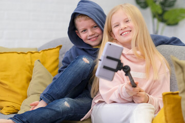 Kids bloggers talking with followers, live streaming looking to smartphone screen at home. Little...