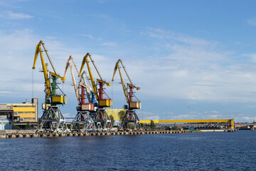 Fototapeta premium Several cargo cranes stand on the banks of the Venta River. Ventspils, Latvia, Baltic Sea. Copy space