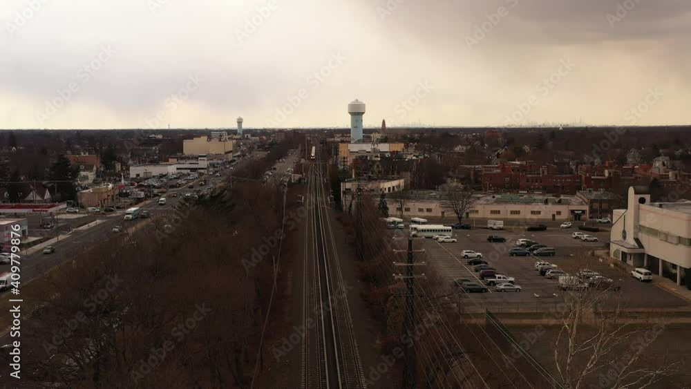 Poster an aerial view over railroad tracks on a cloudy day. a train approaches in the distance and the came