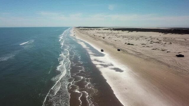Aerial drone view of vehicle driving on beach at low tide on a gulf coast barrier island on a sunny afternoon - South Padre Island, Texas