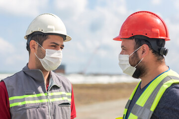 Occupational safety and health specialist and construction worker are talking about pandemic (coronavirus) with protective mask for coronavirus (covid-19) in the construction site.