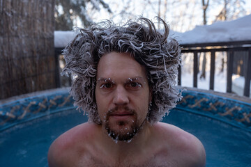 Person, caucasian man sitting in a warm hot tub with frozen , frosted hair during winter season in...