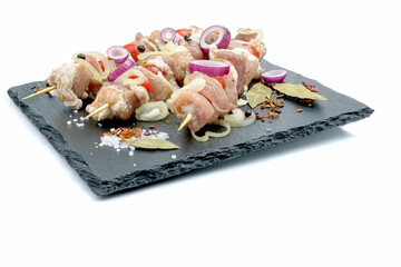 Raw pieces of pork shish kebab in marinade with pepper, onion,bay leaf.Pork kebab, ready to cook, barbecue, isolated on a white background.Selective focus.