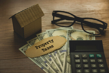 Selective focus of pen.glasses,calculator,money and cardboard home written with Property Taxes on wooden background.