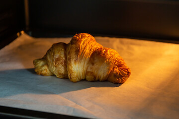 Croissants on heat-resistant paper in the oven with a black background.