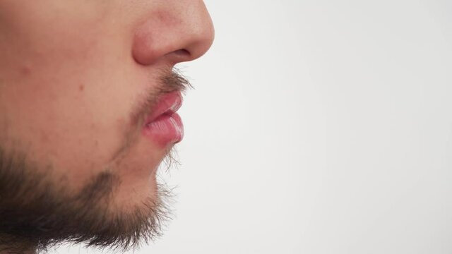 Close up view of alone man mouth with dark brown beard, mustache, large nose, pink lips painted with woman's lipstick on white background. Manifestation of homosexuality of female qualities in men