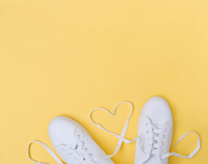 white sneackers with heart shaped laces on yellow background. love concept. blogging content....