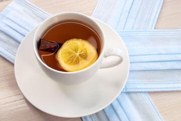 A cup of tea with a slice of lemon and cinnamon is on the medical mask. The concept of prevention against viruses