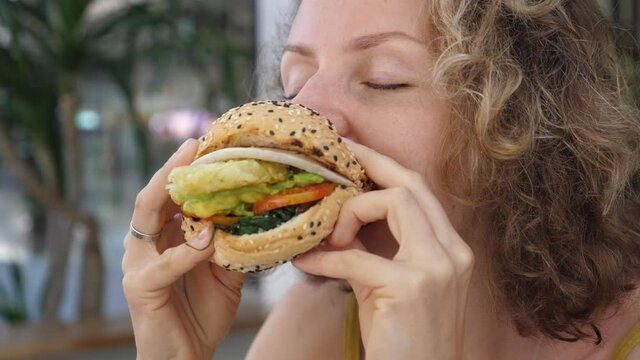 Close up of hungry Caucasian woman taking bite of delicious vegan burger with great appetite 