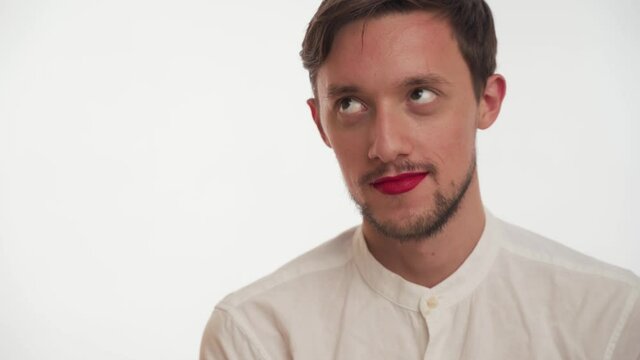 Portrait of young pensive Caucasian metrosexual man with beard, short brown hear, painted lips by red women lipstick wear shirt, stare up, swinging in front of the camera on white background close up.