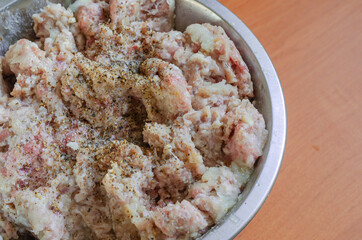 Raw minced meat with grated onion, salt and black pepper in a metal bowl.