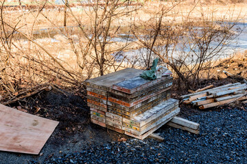 Metal forms for concrete work stacked in front of branches with frozen river in background.