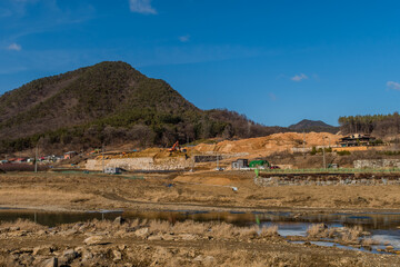 Landscape of river, mountains and construction site under beautiful blue sky.