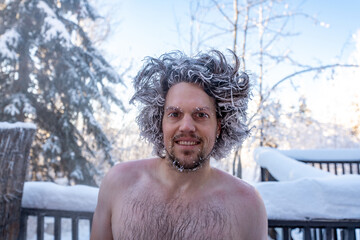 Man standing with winter background, blue sky and trees with hair totally frozen, white tips and...
