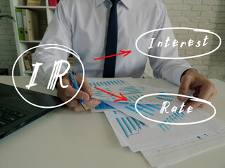 Business concept about IR Interest Rate with handwritten acronym.Busy businessman under stress due...