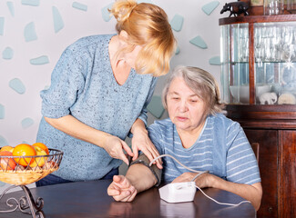 A young woman measures the blood pressure of an elderly woman