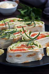 Rolls of thin pita bread and red salted salmon with lettuce leaves on a black ceramic plate, dark wooden background.