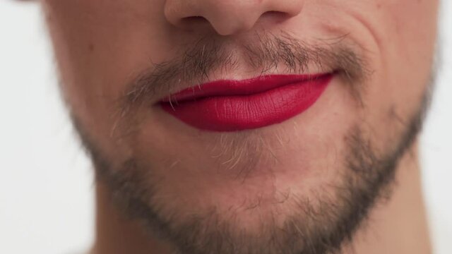 Close-up view of cute Caucasian male mouth with beard and moustache. Man wear red lipstick on lips, blow kiss on white background. Concept of protecting rights of LGBT community, clear manifestation