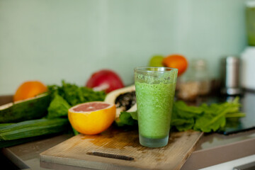 A green smoothie is on the table, next to fresh vegetables and fruits