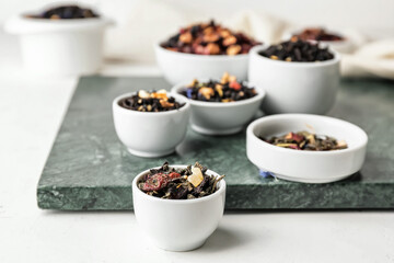 Bowls with different types of dry fruit tea on light background