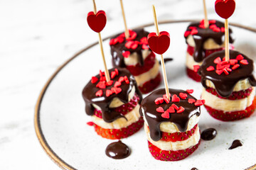  Banana and strawberry canapes in chocolate glaze on a white plate, an original appetizer for Valentine's Day