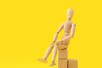 Wooden mannequin sitting on wooden cubes against color background