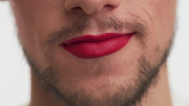 One Bearded Man wear red lipstick on lips Pulls his lips forward in tube, makes blow kiss gesture isolated on white background close up. Mouth of fashion boy, likes to do makeup with women's cosmetics
