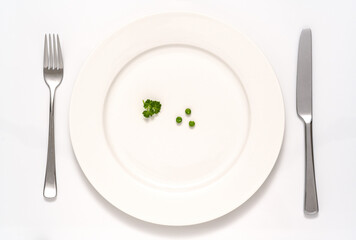 Drei Erbsen und etwas Petersilie auf einem weissen Teller mit Messer und Gabel