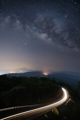 Night sky with milky way and stars. Night road illuminated by car. Light trails
