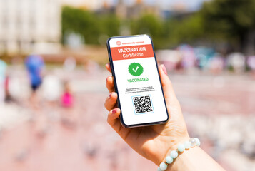 Woman outdoors in city holding mobile phone with valid digital vaccination certificate