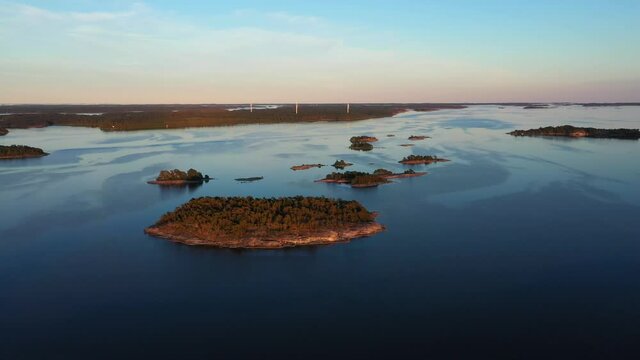 Aerial drone view over small islands towards wind power turbines, sunset, in the Archipelago of Scandinavia