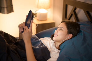 A young woman is using tablet , watching movies or video call to her friends or family in her bedroom , night Light.