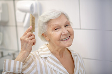Gray-haired woman brushing her hair in the bathroom and feeling good