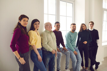 Group of people of different ages and nationalities is standing by a large window. Grandchildren...