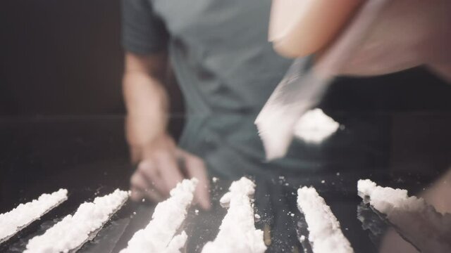 Cocaine addict cutting lines of white powder with a razor blade, US dollar bill.