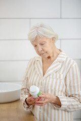 Short-haired old lady holding a bottle with vitamins in her hands