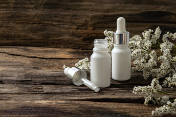 White cosmetic bottles and dropper with white small flowers  on wood background. Blank label for branding mock-up.