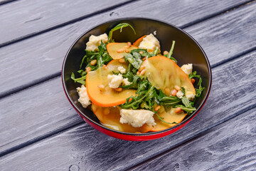 Arugula salad, persimmon, walnuts, avocados, feta cheese on a white plate on a wooden table