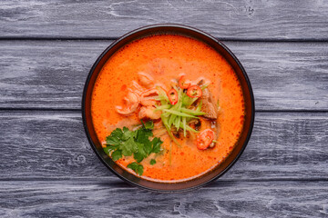 Soup with seafood and shrimps served in a black bowl over rustic wooden background.