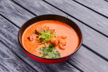 Soup with seafood and shrimps served in a black bowl over rustic wooden background.
