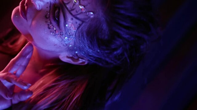 Portrait of a beautiful woman with an unusual pattern and with rhinestones on her face posing in front of the camera in the studio against the background of curtains. Makes beautiful hand movements.